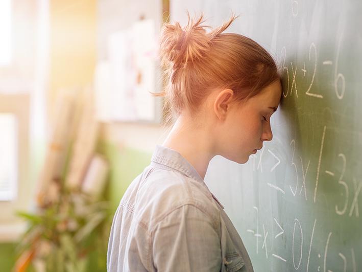 A student rests her forehead against a blackboard of math equations.