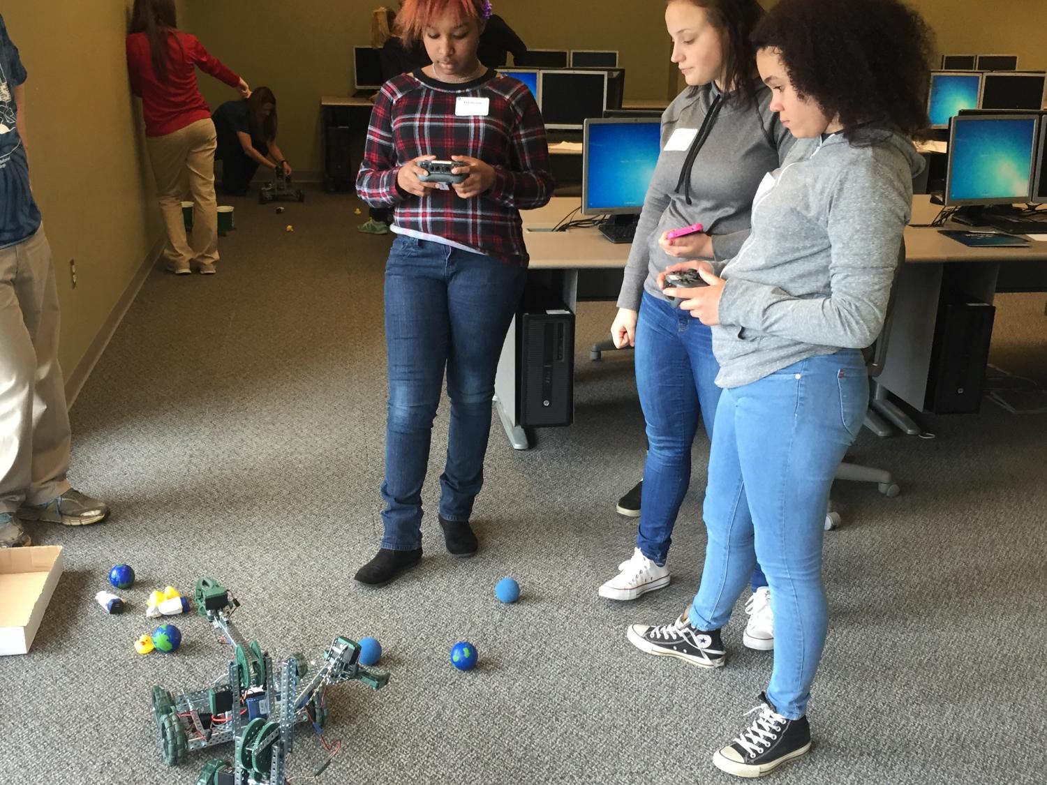 Asialynn Noyer, left, and Mariah Lucas, far right, both control VEX robots while Ashja Raucci, center, looks on.