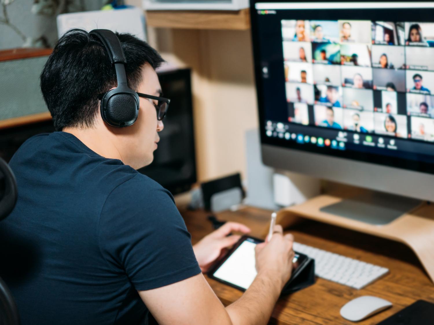 A male student wearing headphones participates in a virtual class