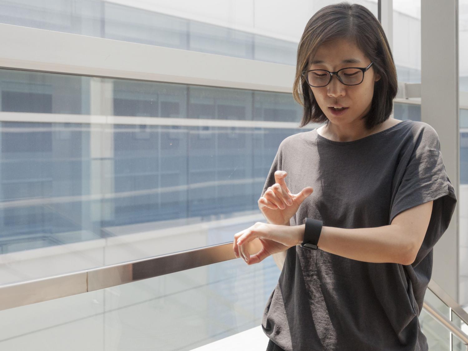 A woman in a gray top looks at the FitBit monitor on her wrist