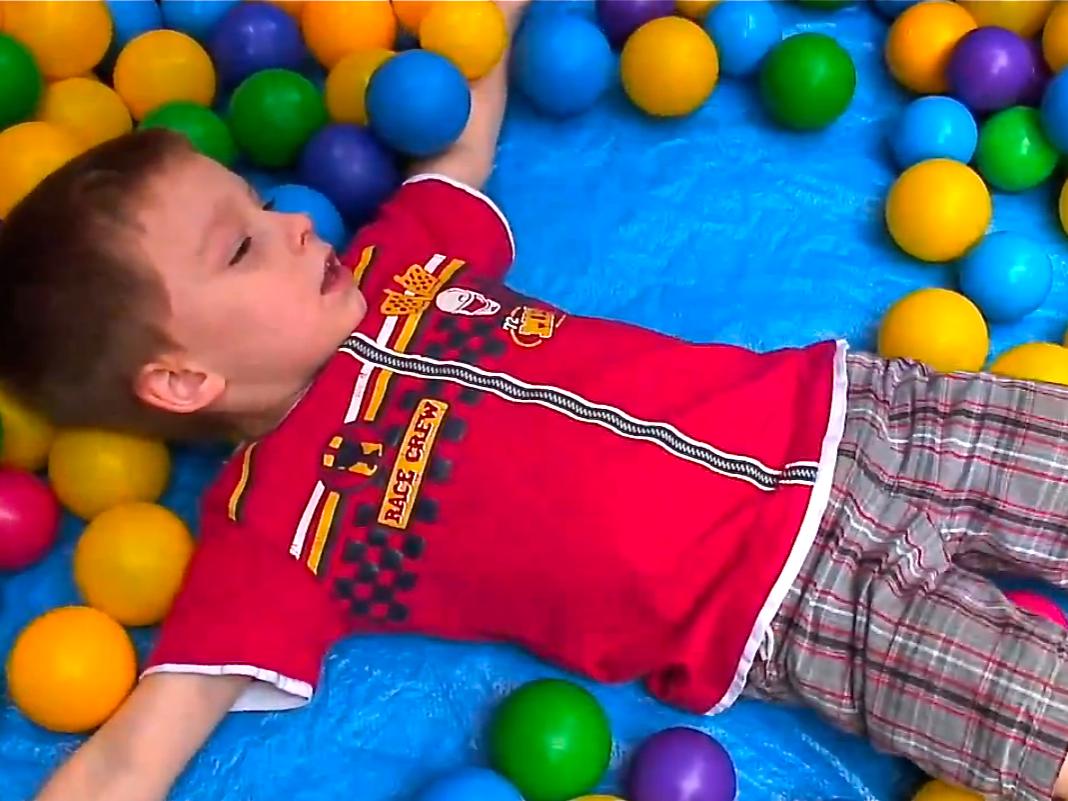child in play area surrounded by multiple colors of plastic balls