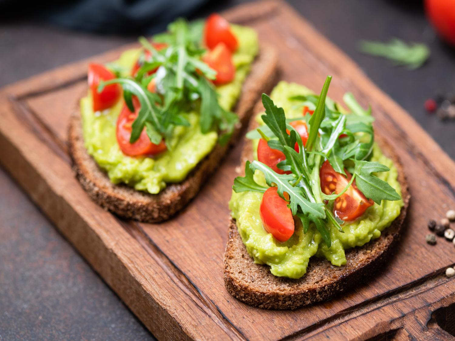 A cutting board with two pieces of avocado toast on it
