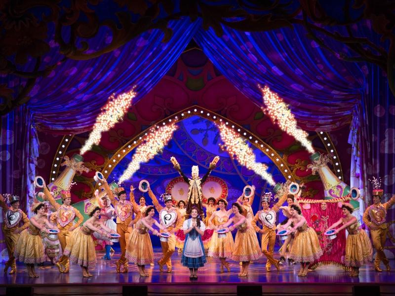 The ensemble cast, dressed in colorful costumes and against an intricate backdrop, sings "Be Our Guest" in "Disney's Beauty and the Beast."