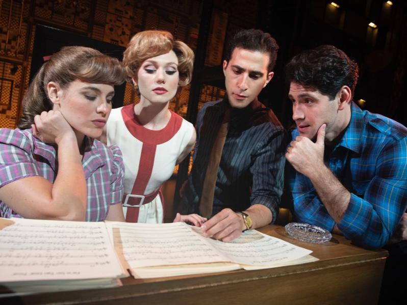 Two women and two men sit at a table while they look at sheet music.