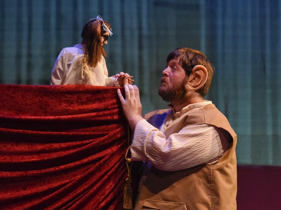 The Big Friendly Giant speaks with his new human friend Sophie while she, in miniature puppet form, stands behind a curtained podium.