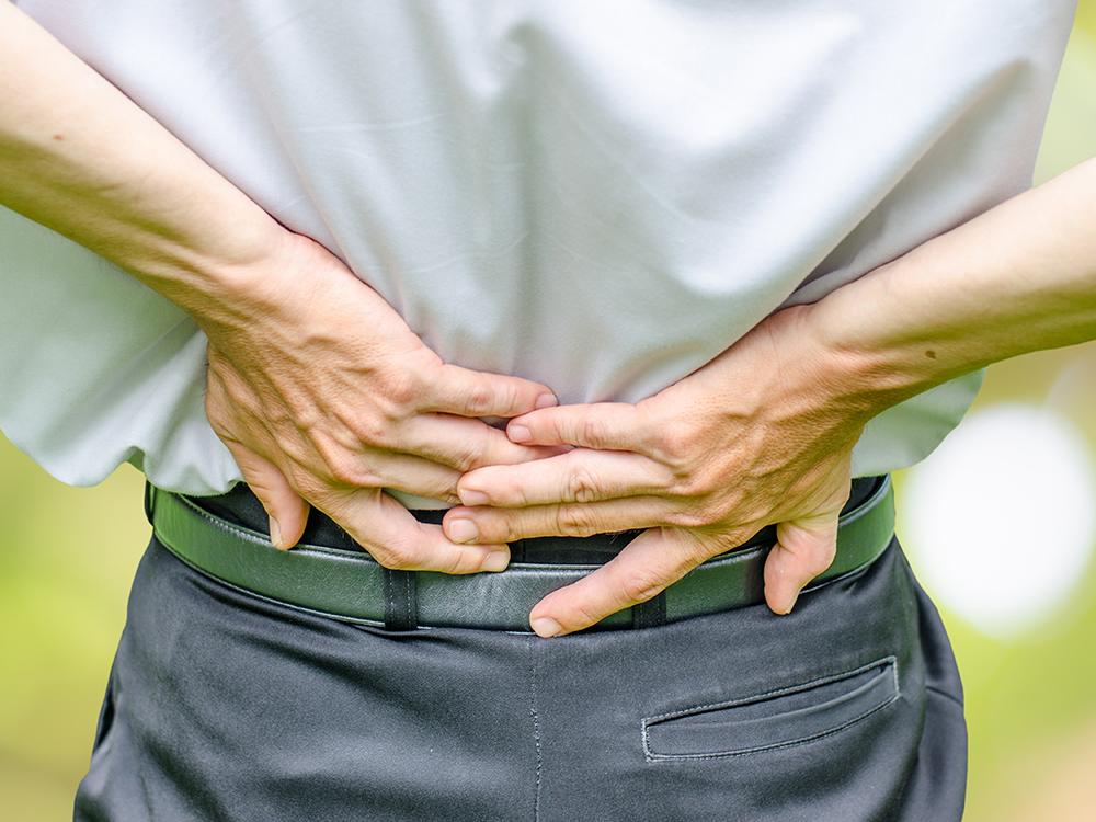 Close-up view of a man putting his hands on his lower back.