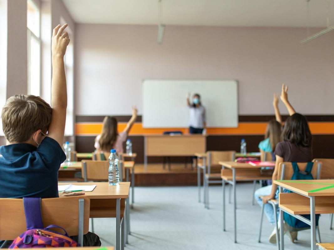 Students with protective masks sitting in school desks in their classroom. School desks are marked with a cross to mark a place where sitting is not allowed to maintain social distance during the COVID-19 pandemic.