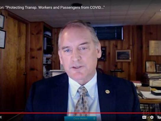 A screengrab of a white man in a tie and jacket speaking from a wood-paneled home office. 
