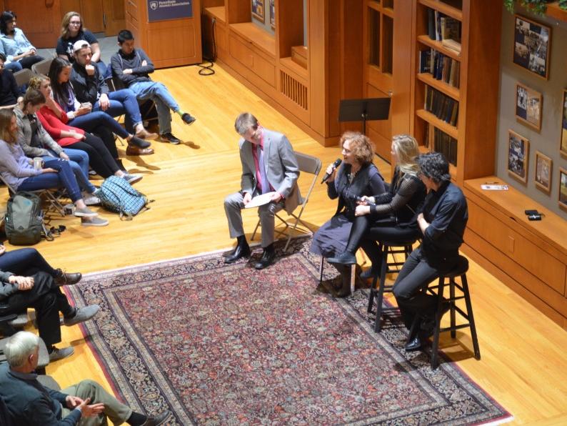 Four musician-artists sit on stools in front of a seated audience.
