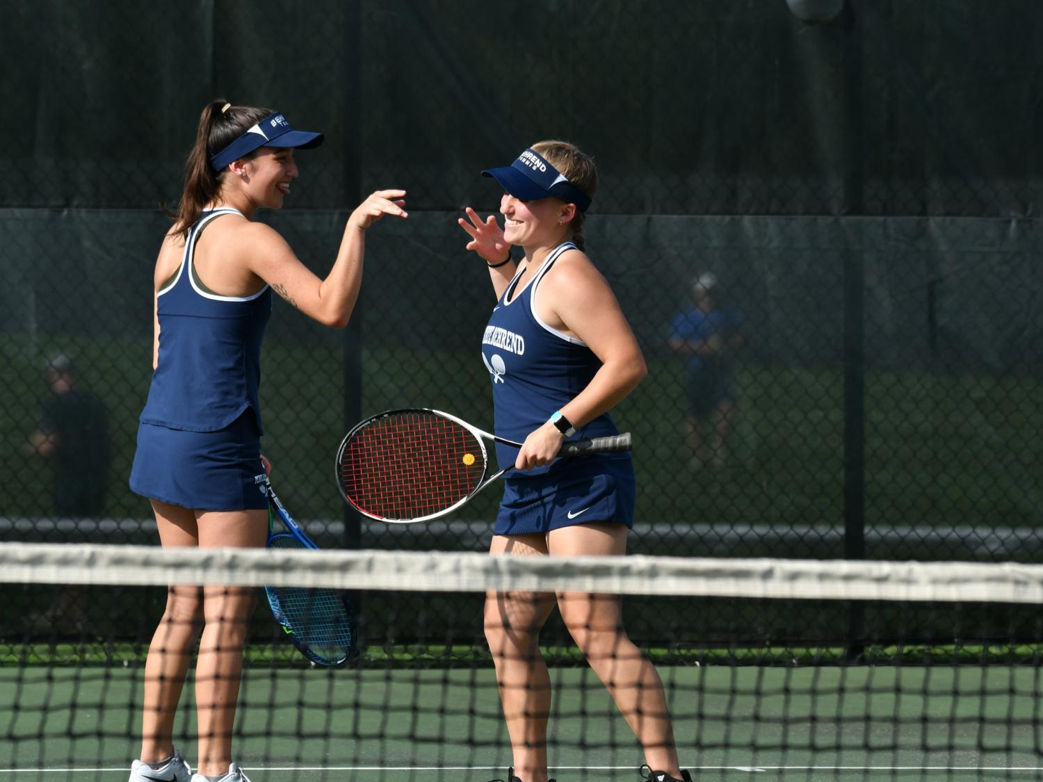 Two Penn State Behrend tennis players congratulate each other after winning a point.
