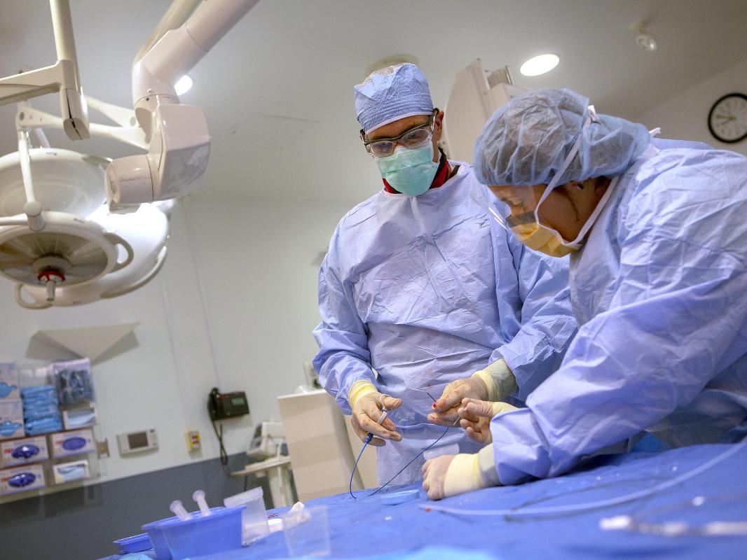 Two medical professionals wearing blue scrubs, facemasks and gloves perform a biopsy on a heart transplant patient at Penn State Health Milton S. Hershey Medical Center.