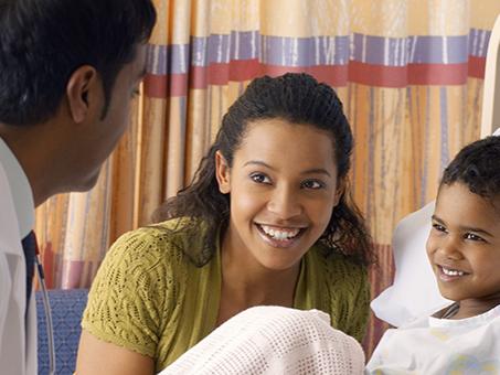 A physician talks with a patient and his mom at the bedside.