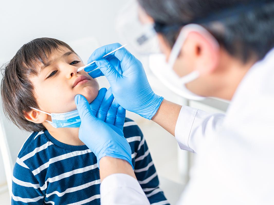 A doctor administers a nasal swab to a young boy, who is being tested for COVID-19.