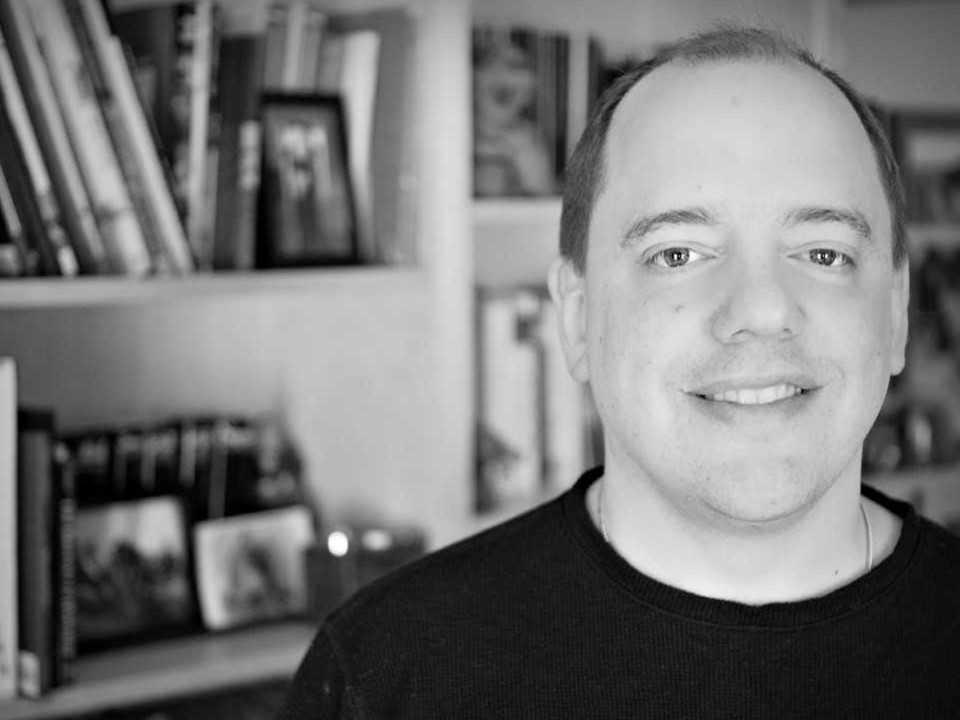 Photo of Brad Ricca in front of a book case.
