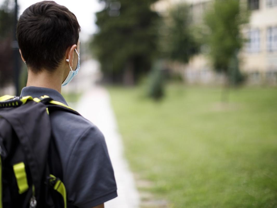 Rear view of school teenage boy with face protective mask in front of the school.
