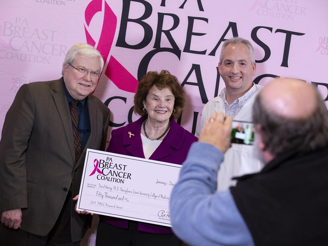 Three people post for a photo while holding a big check.