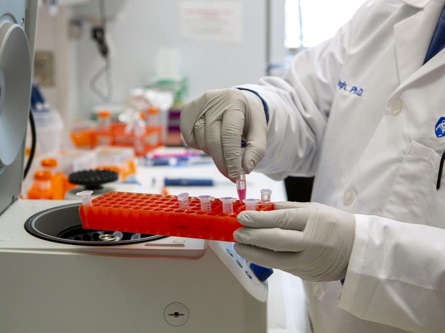 A worker in a lab coat works with small tubes in a lab.