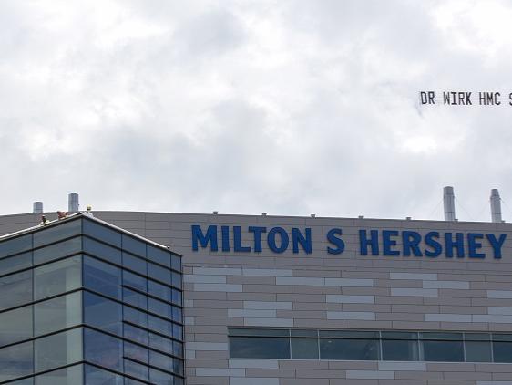 A plane flies in the sky above Hershey Medical Center, trailing a banner.