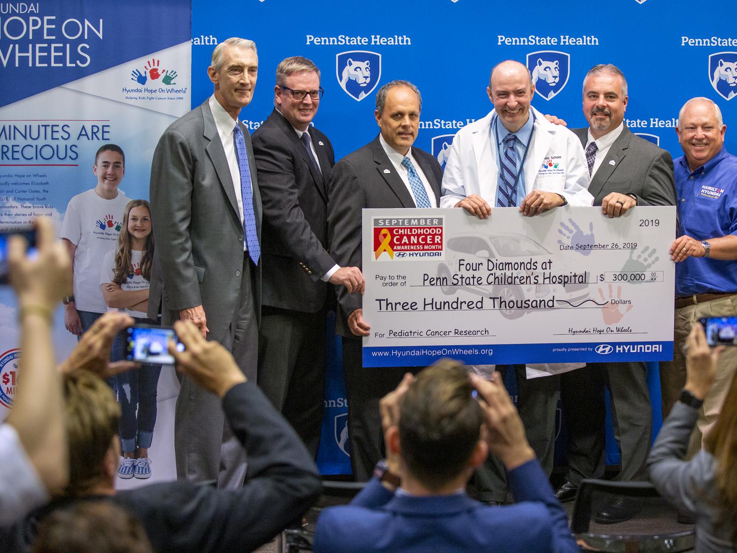 Six men smile for a photo while holding a big check.