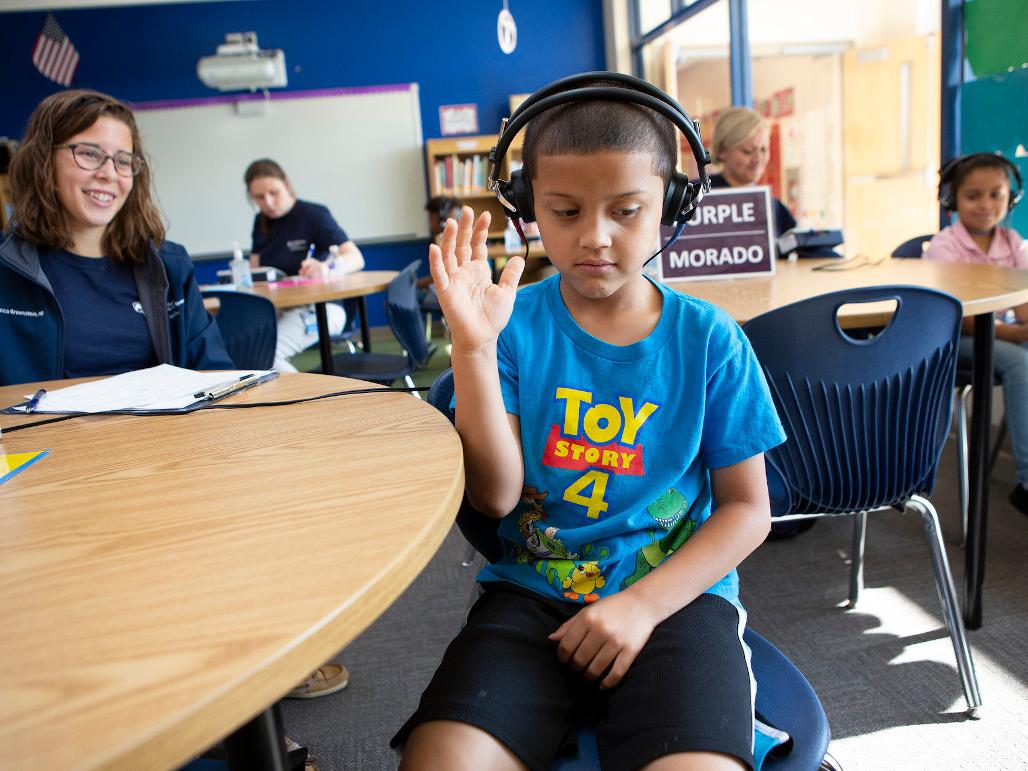 A boy wearing headphones raises his arm while doing a hearing test