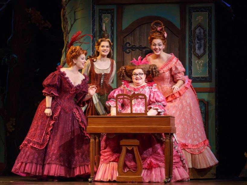 Actresses portraying Cinderella and her evil stepsisters stand in a semicircle around a seated stepsister.