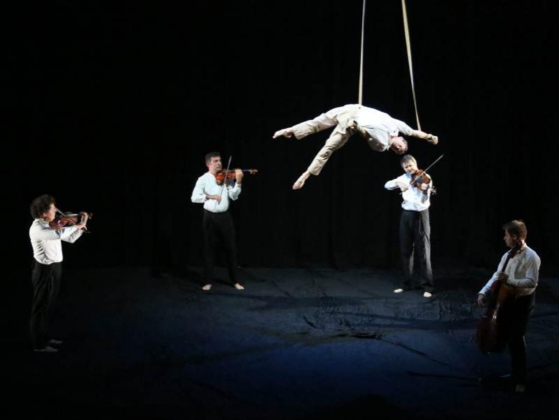 The musicians of Dubussy String Quartet perform in a circle while an acrobat dangles from a rope in the middle of them in Circa "Opus."