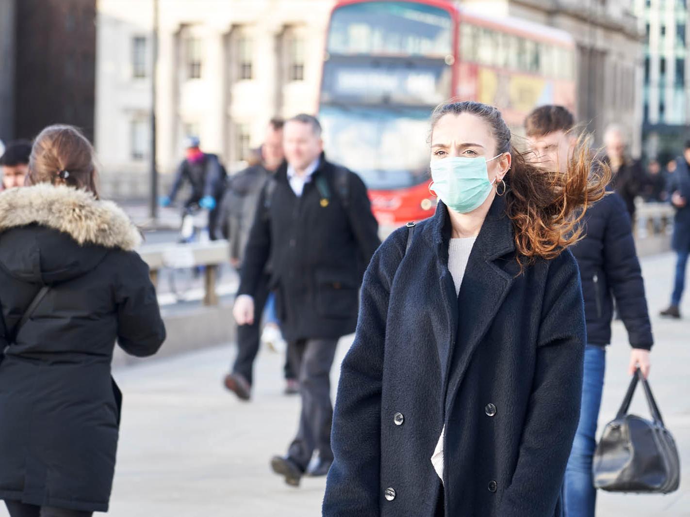 Several people walk along a busy city street. Some have on face masks, others do not.