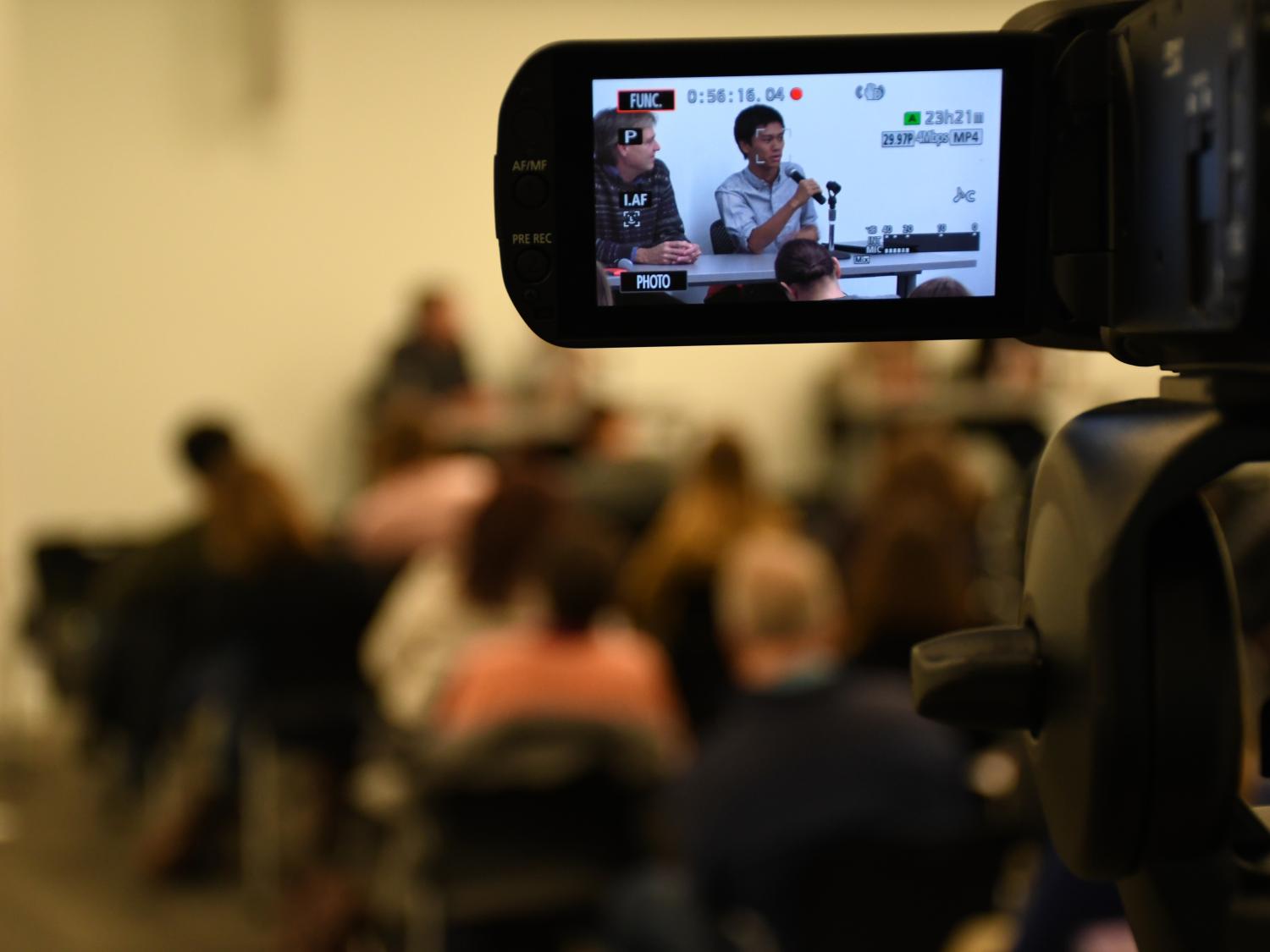 Freelancer Angus Chen addresses the crowd, as seen through a camera's viewfinder.