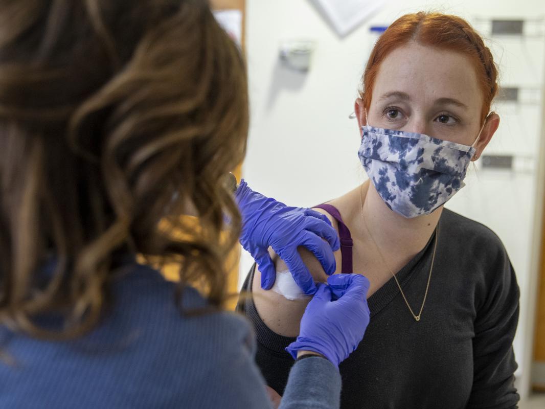 A nurse places a bandage on the right arm of a woman after having given her a shot.
