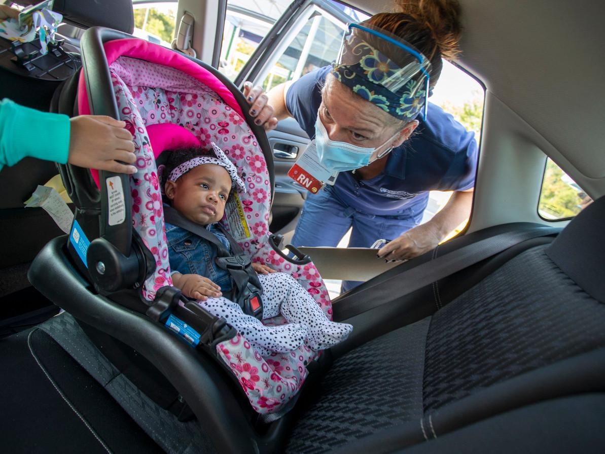 A woman helps adjust a child's car seat