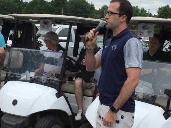 A man standing by a golf cart talking with a microphone.
