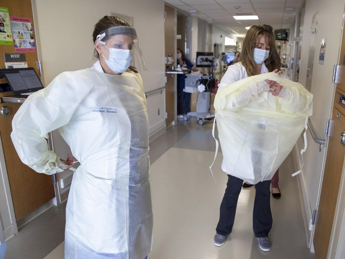 Two women don personal protective equipment in a hospital hallway.