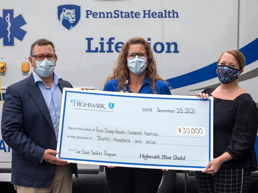 Three people pose for a photo while holding a big check
