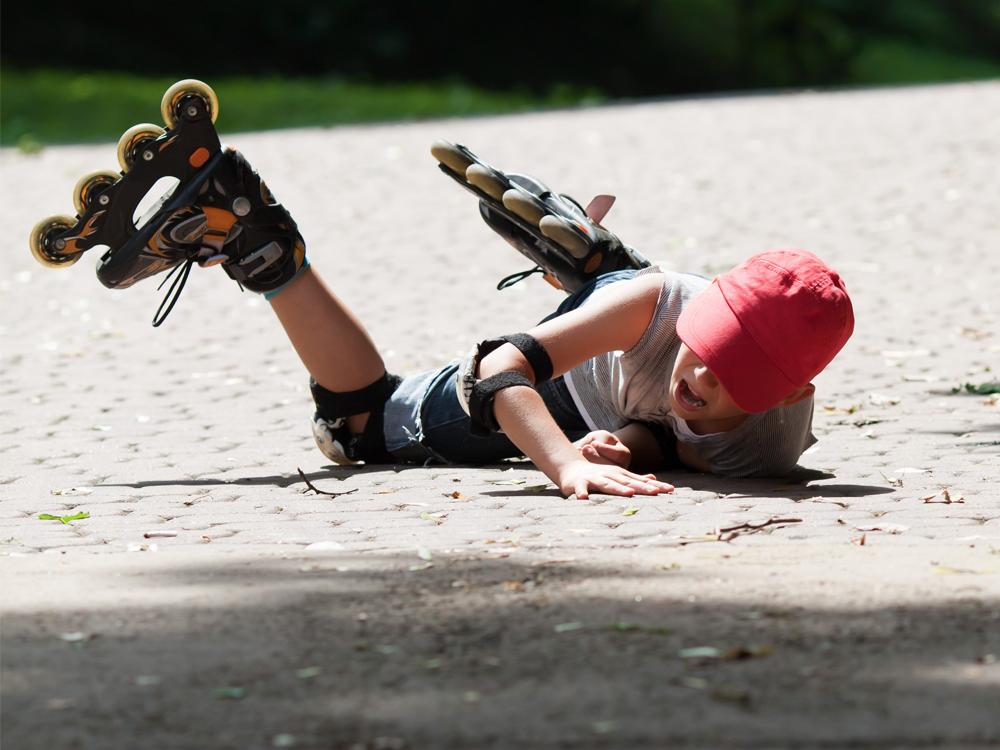 A child wearing roller blades lays on a brick driveway, apparently after falling.