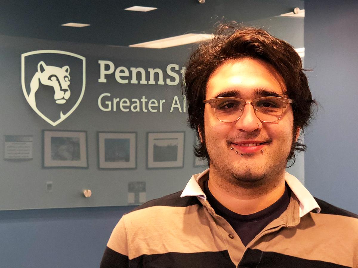 Christian L. Villanueva smiles in front of Penn State Greater Allegheny Logo