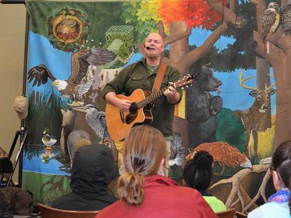 A musician plays his guitar on the stage in front of a colorful background.