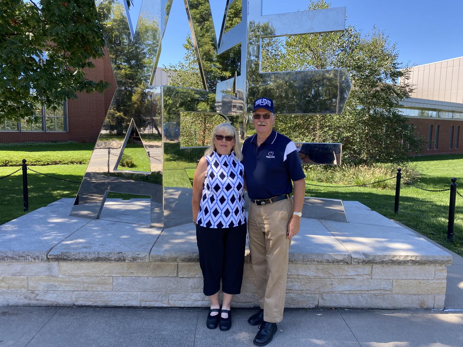 A couple standing in front of the WE ARE statue at University Park