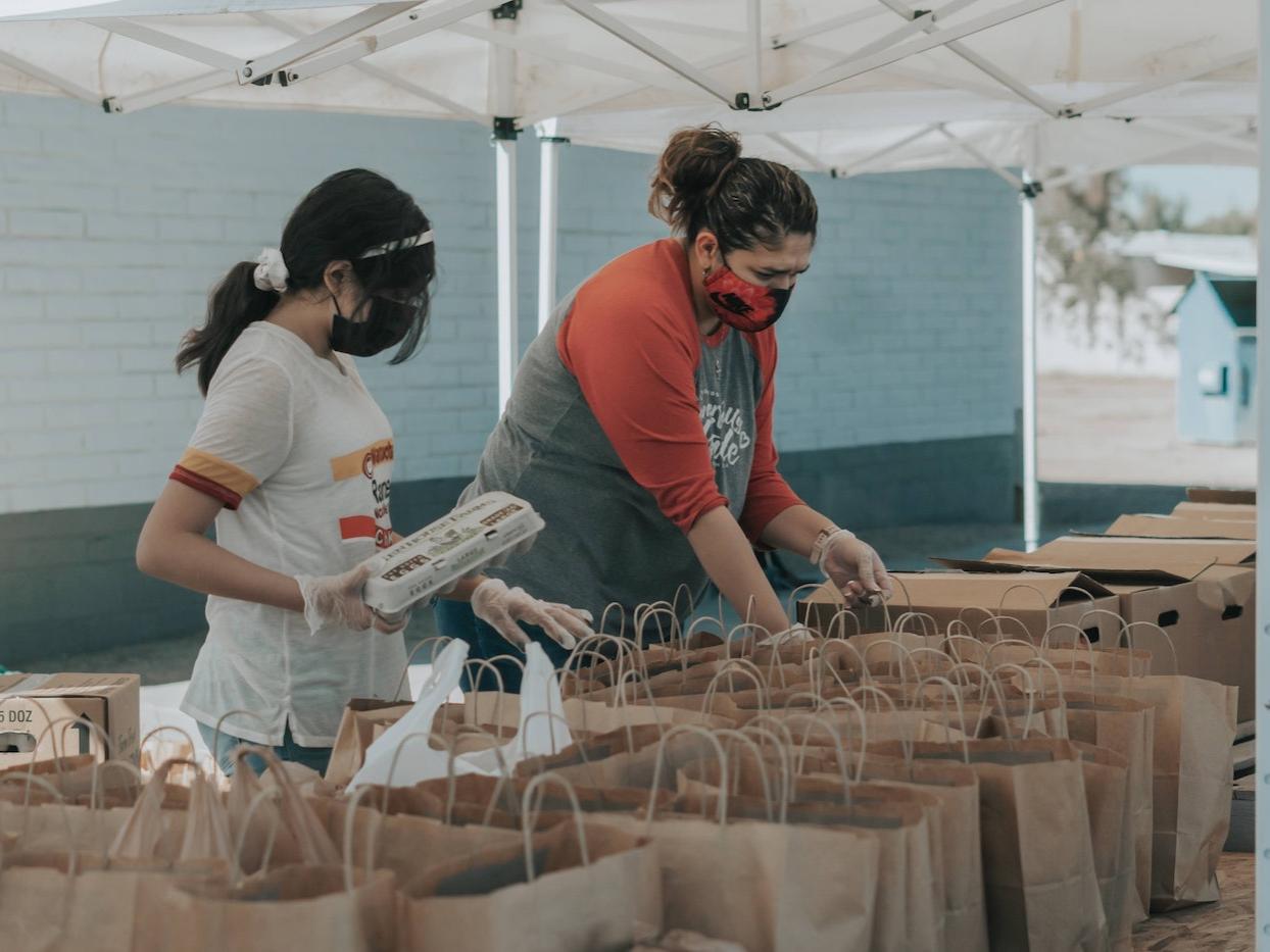 Two people packing paper bags with food.