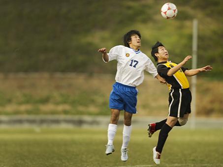 Two soccer players jump to try to head a soccer ball.