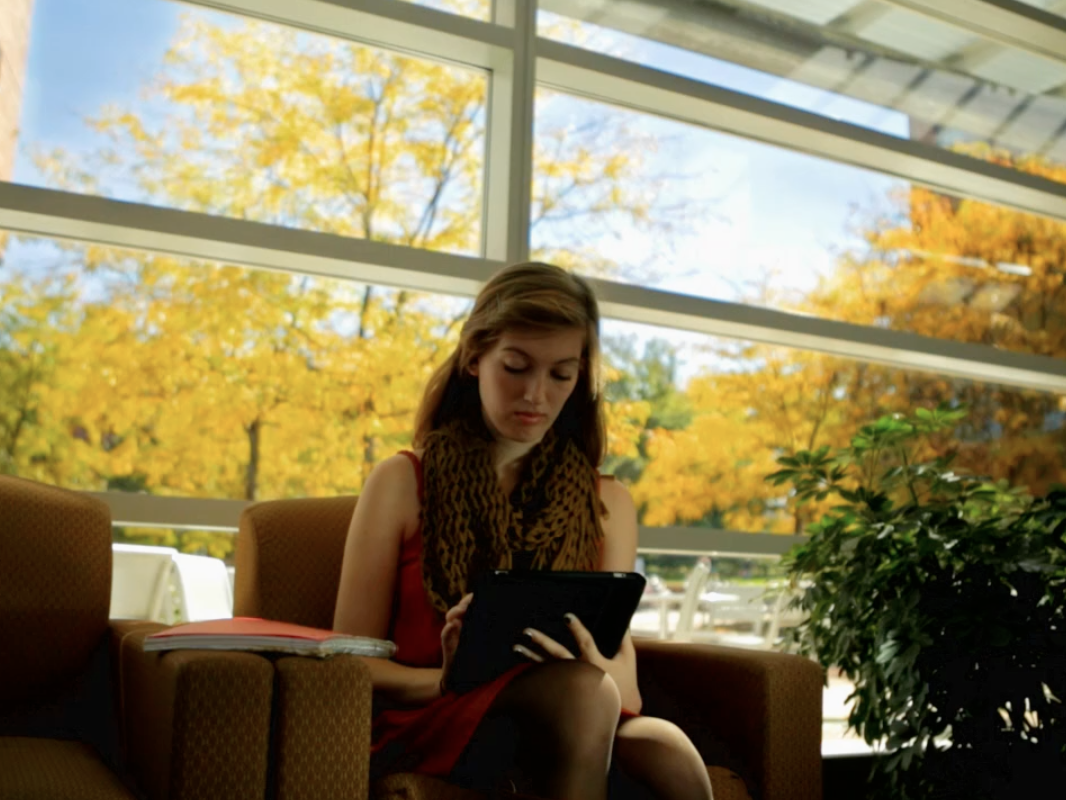 A student sitting in a chair uses a tablet computer