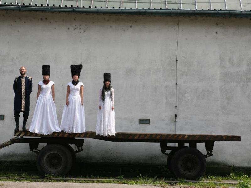 Members of the band DakhaBrakha—a male musician wearing a traditional Ukrainian suit and three women dressed in traditional wedding dresses and headgear—stand on the flatbed of a truck trailer.