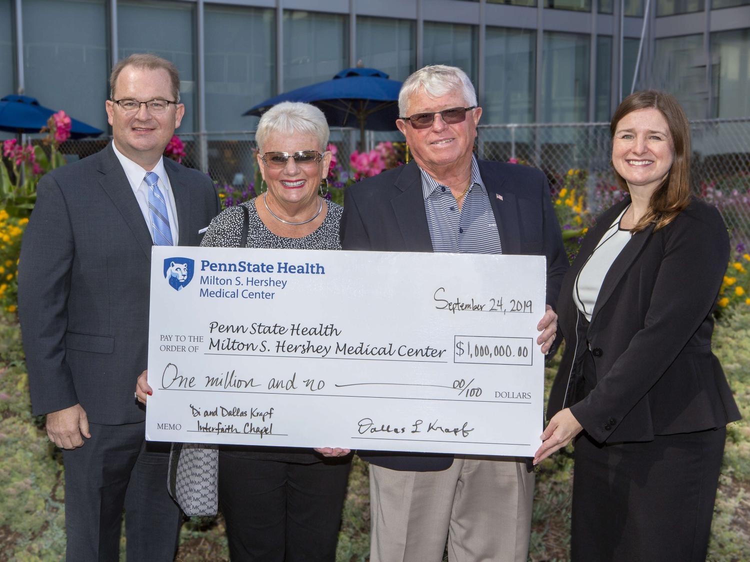 Four people – two men and two women – pose outside for a photo holding an oversized check made out to Penn State Health Milton S. Hershey Medical Center, in the amount of $1 million. It’s signed by Dallas Krapf. 