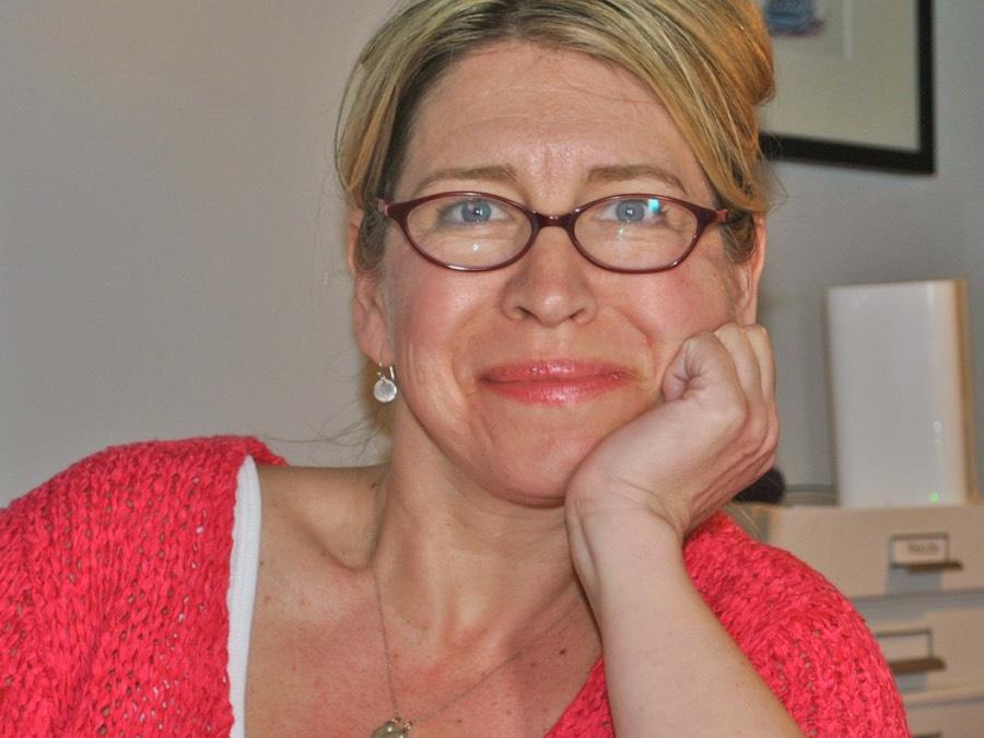 A woman rests her chin in her hand while she smiles at the camera.
