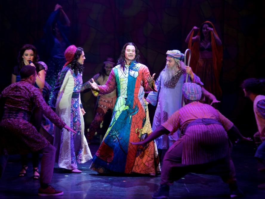 Joseph, wearing his coat of many colors, sings to a crowd of shepherds in “Joseph and the Amazing Technicolor Dreamcoat.” 