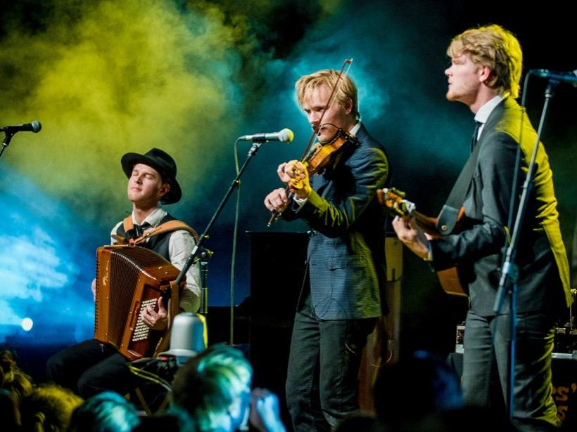 Three musicians stand on stage and play their instruments.