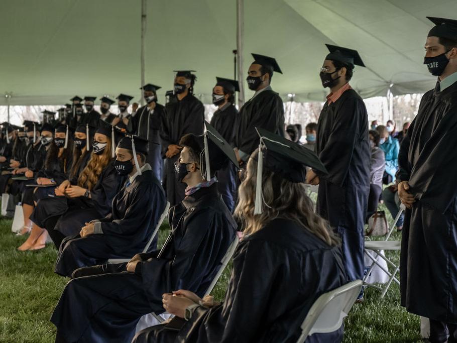 Row of graduates in caps and gowns seated in front of another row of graduates standing.