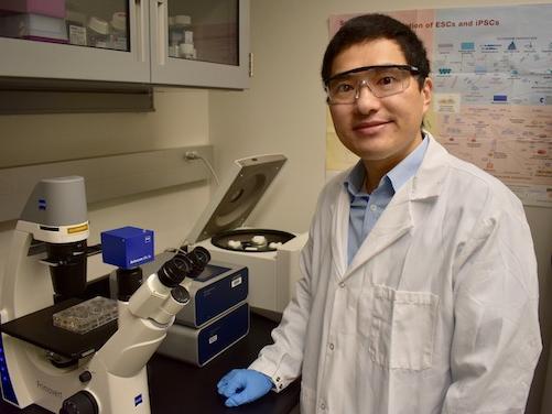 Man in lab coat standing next to a microscope