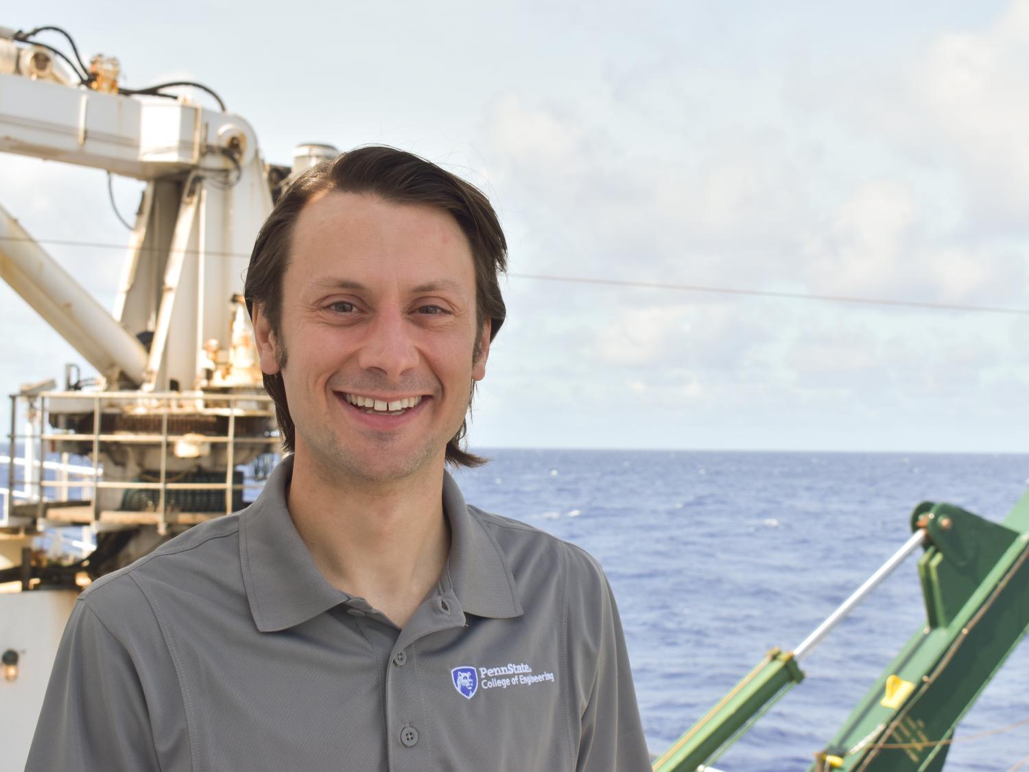 A man in a polo shirt stands on a boat in front of the ocean. 
