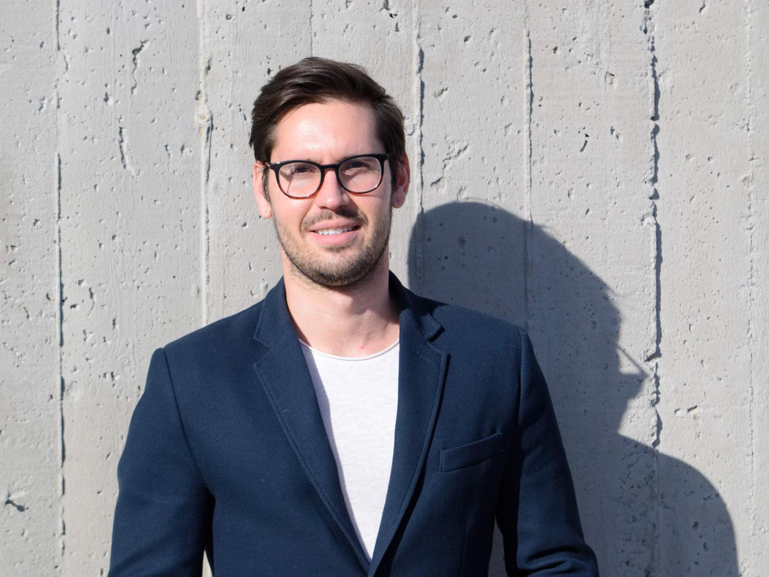 casual photo of head, shoulders and chest of fair-skinned, dark haired, younger man with dark-rimmed glasses.