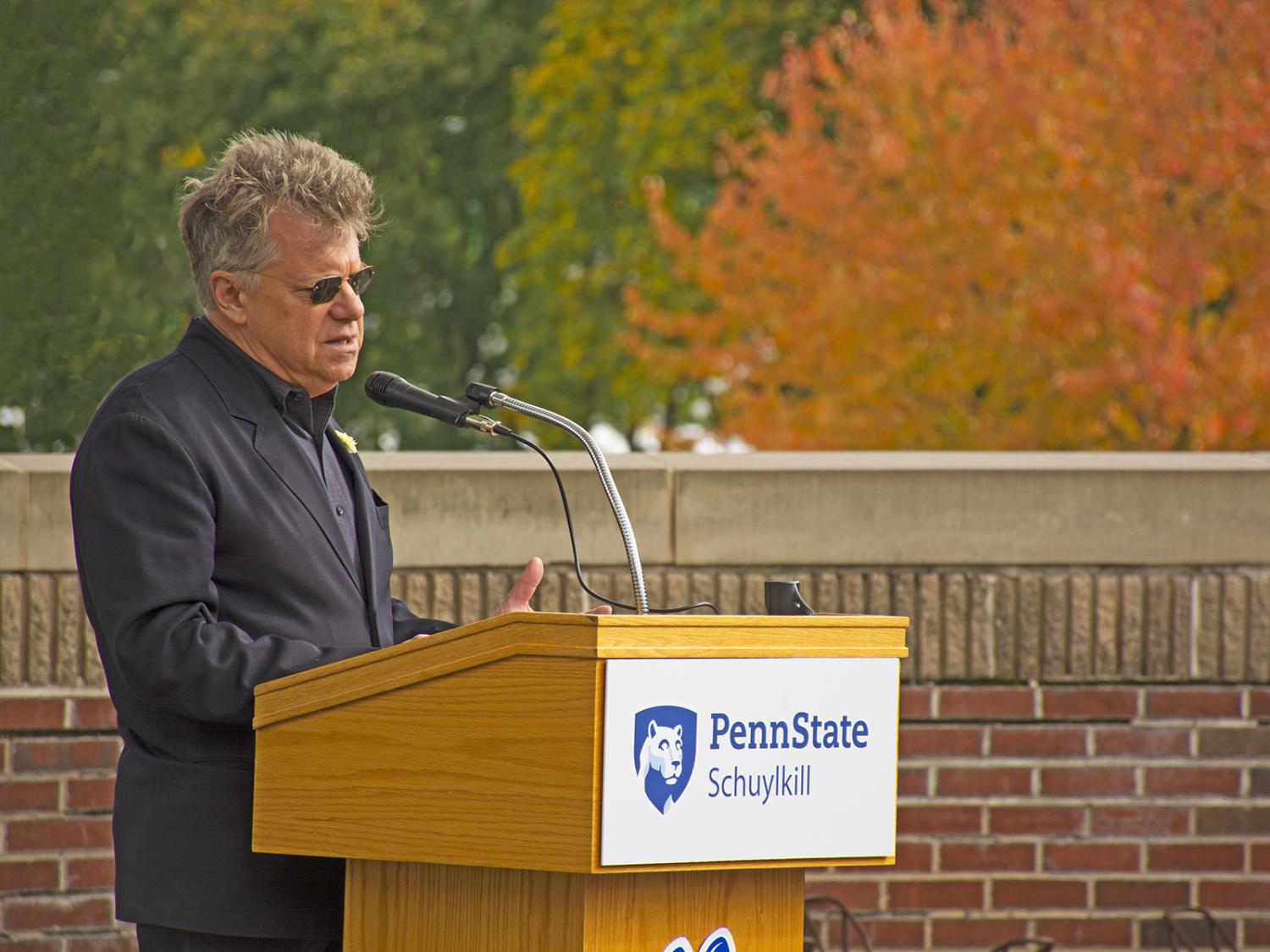A man wearing all black with sunglasses speaks while standing at a podium